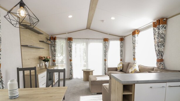 Une cuisine moderne avec une table en bois, des chaises et un banc intégré. On y trouve un coin repas avec une table et des chaises, ainsi qu’un canapé avec des coussins. La cuisine est dotée d’un plan de travail et d’armoires en bois.