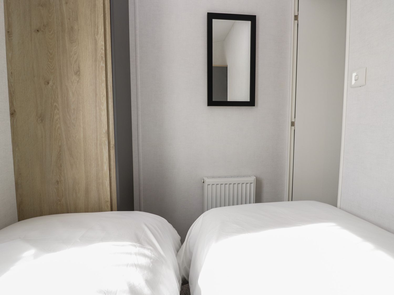Een slaapkamer met twee bedden, een houten deur, een radiator en een spiegel aan de muur.