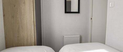 Een slaapkamer met twee bedden, een houten deur, een radiator en een spiegel aan de muur.