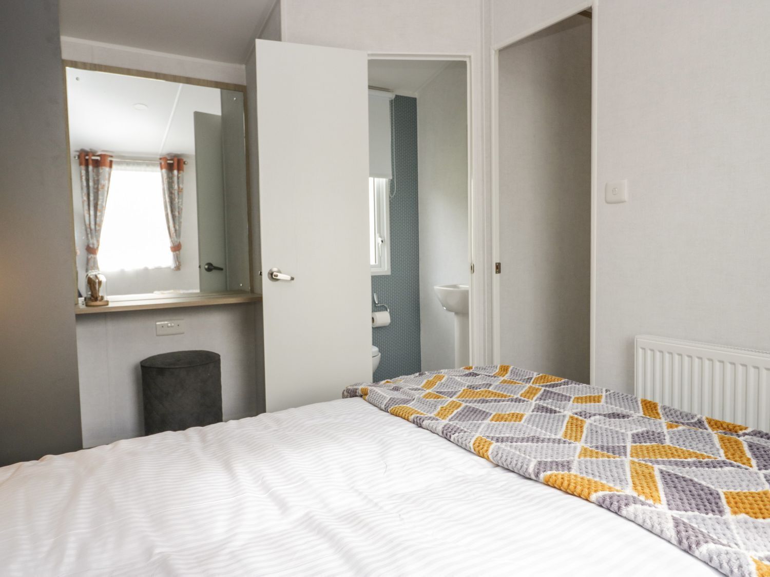 Un dormitorio con cama, espejo, puerta que da a un baño y radiador.