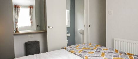 Un dormitorio con cama, espejo, puerta que da a un baño y radiador.