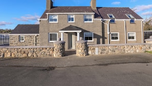 A two-story house with a stone facade, multiple windows, and a chimney. - Ty'n Ffridd Bach (Pwllheli)