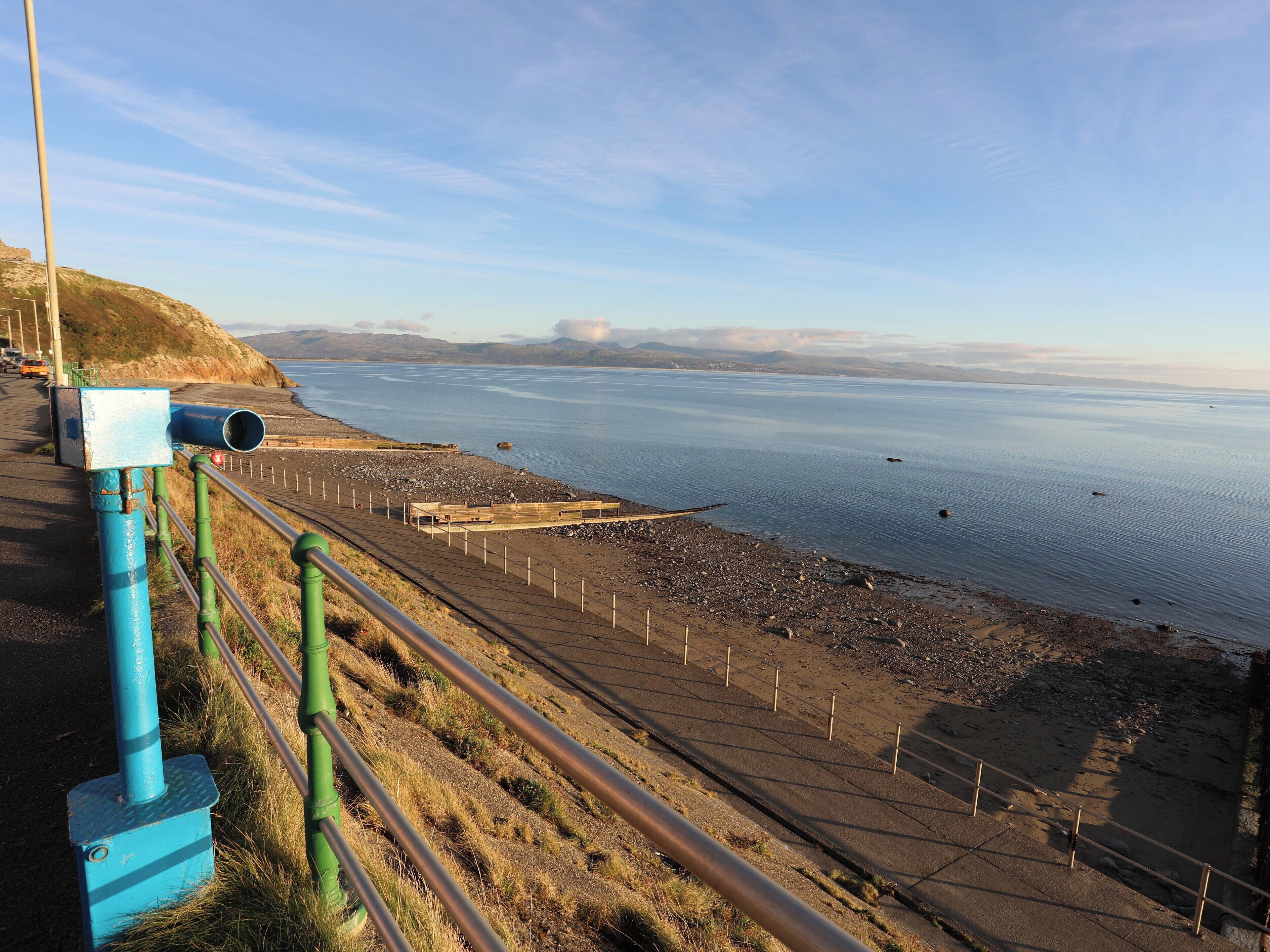 A coastal road with a guardrail, a rocky beach, and a calm sea.