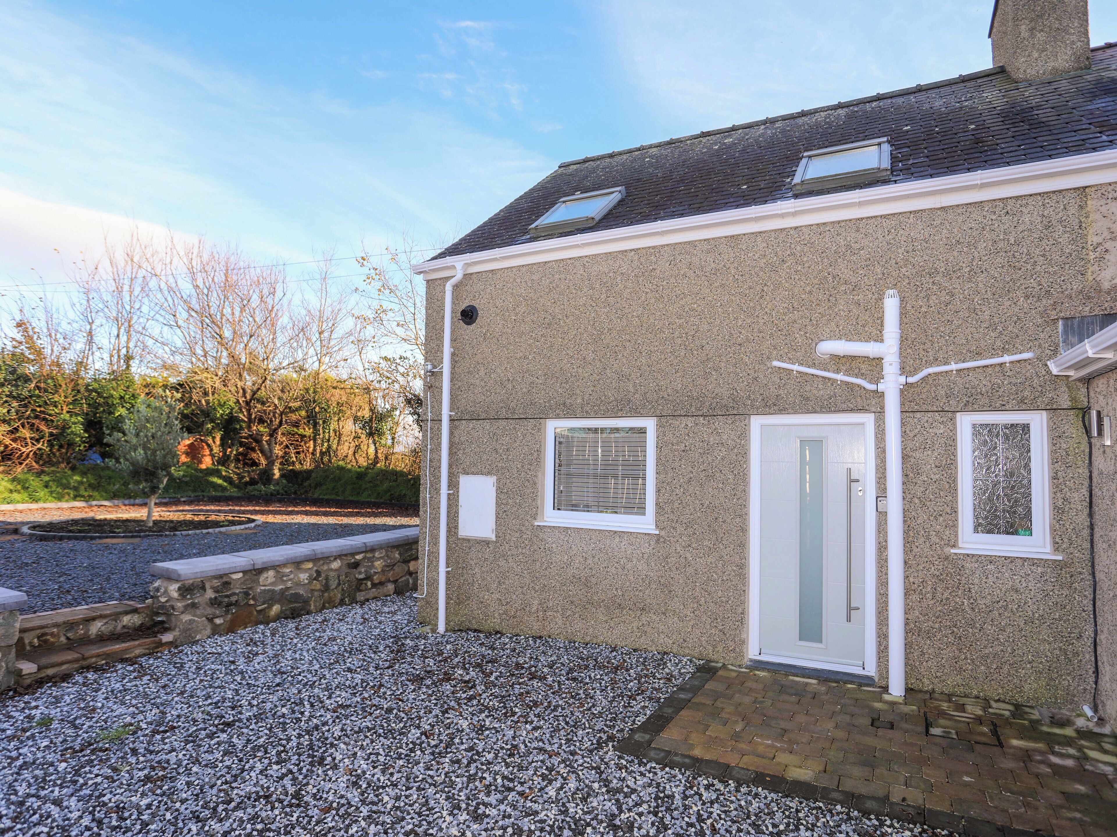 A house with a gravel driveway, a stone wall, and a wooden deck.
