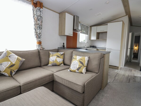A modern living area with a sectional sofa, a kitchen with white cabinets, and a dining area.