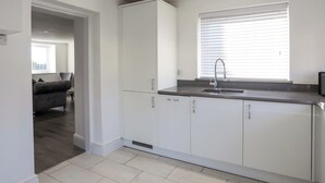 Cocina moderna con armarios blancos, un lavamanos de acero inoxidable y una ventana con persianas.