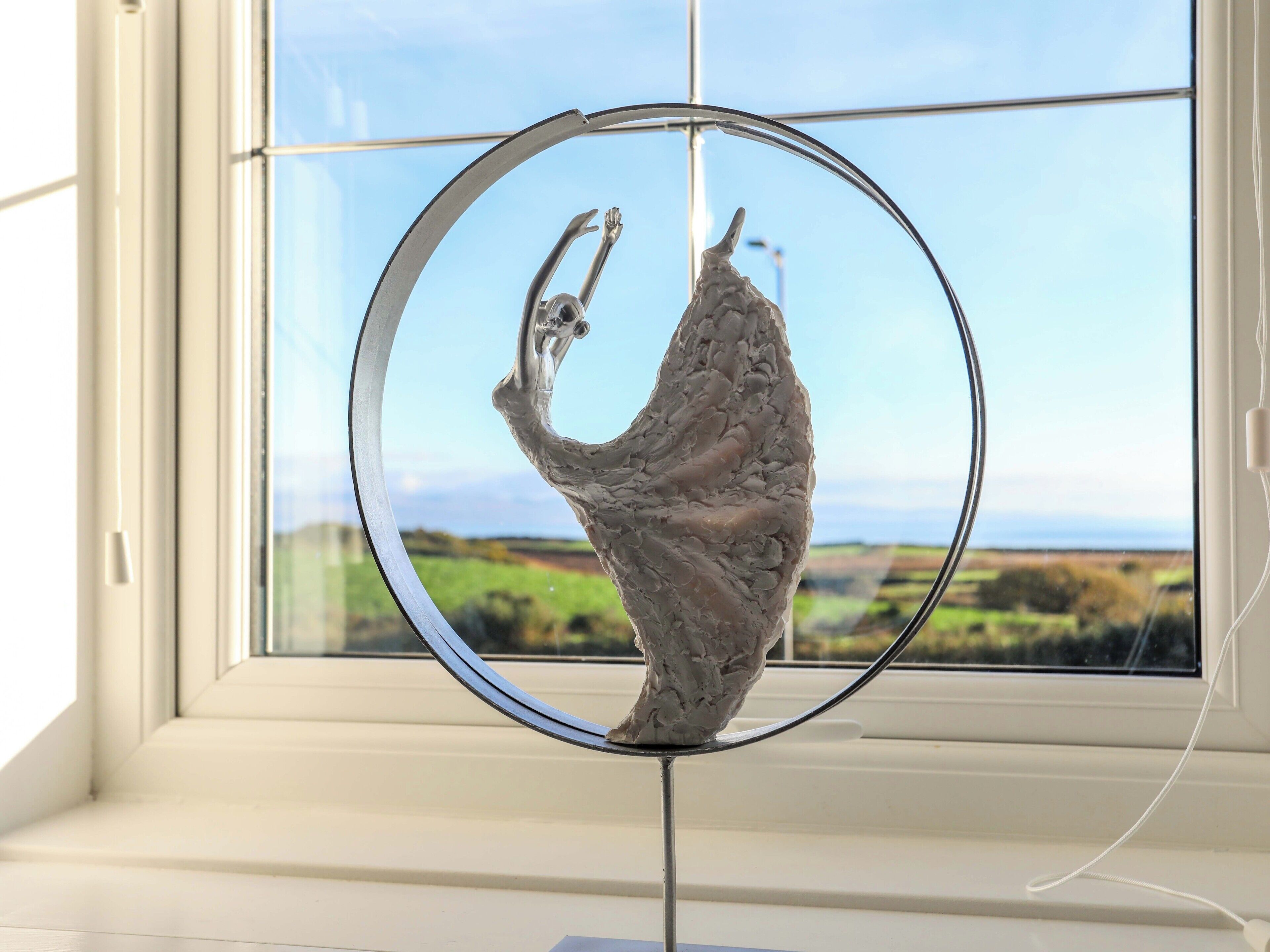 Uma escultura de criatura mítica emoldurada em círculo, posicionada em frente a uma janela com vista para uma paisagem verde.