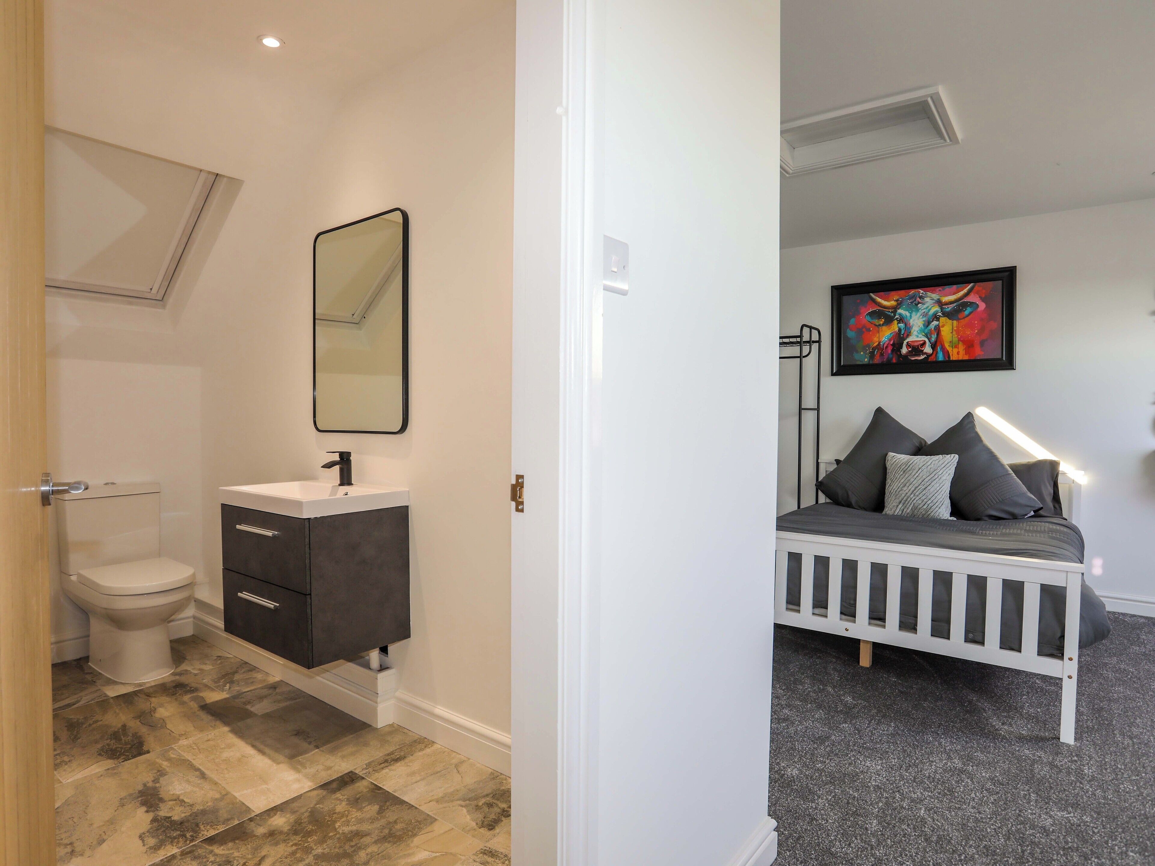 A bedroom with a white crib, a bedside table, and a colorful painting on the wall.