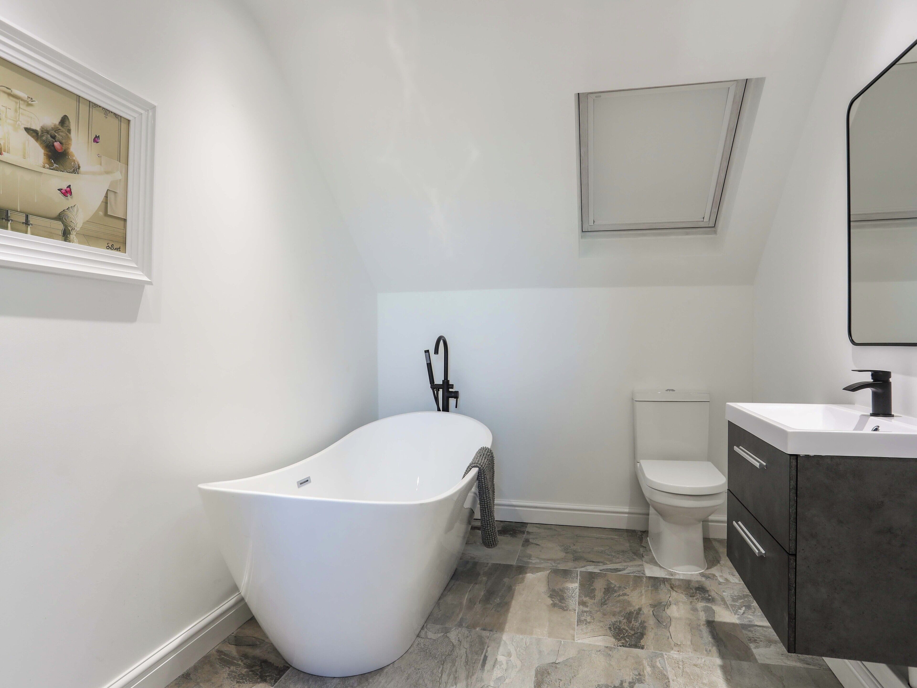 Een moderne badkamer met een vrijstaand bad, een toilet en een wastafel met spiegel.