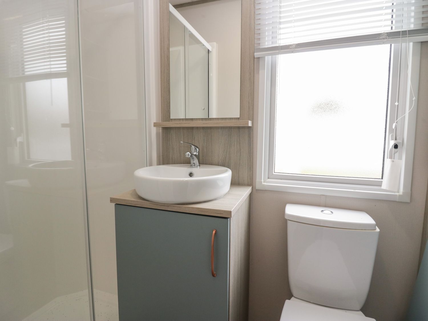 A bathroom with a white sink, a mirror, a toilet, and a window with blinds.