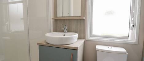 A bathroom with a white sink, a mirror, a toilet, and a window with blinds.