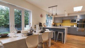 A modern kitchen with a central island, stainless steel appliances, and a view of greenery outside. - 3 Grange Villas (Bridport)
