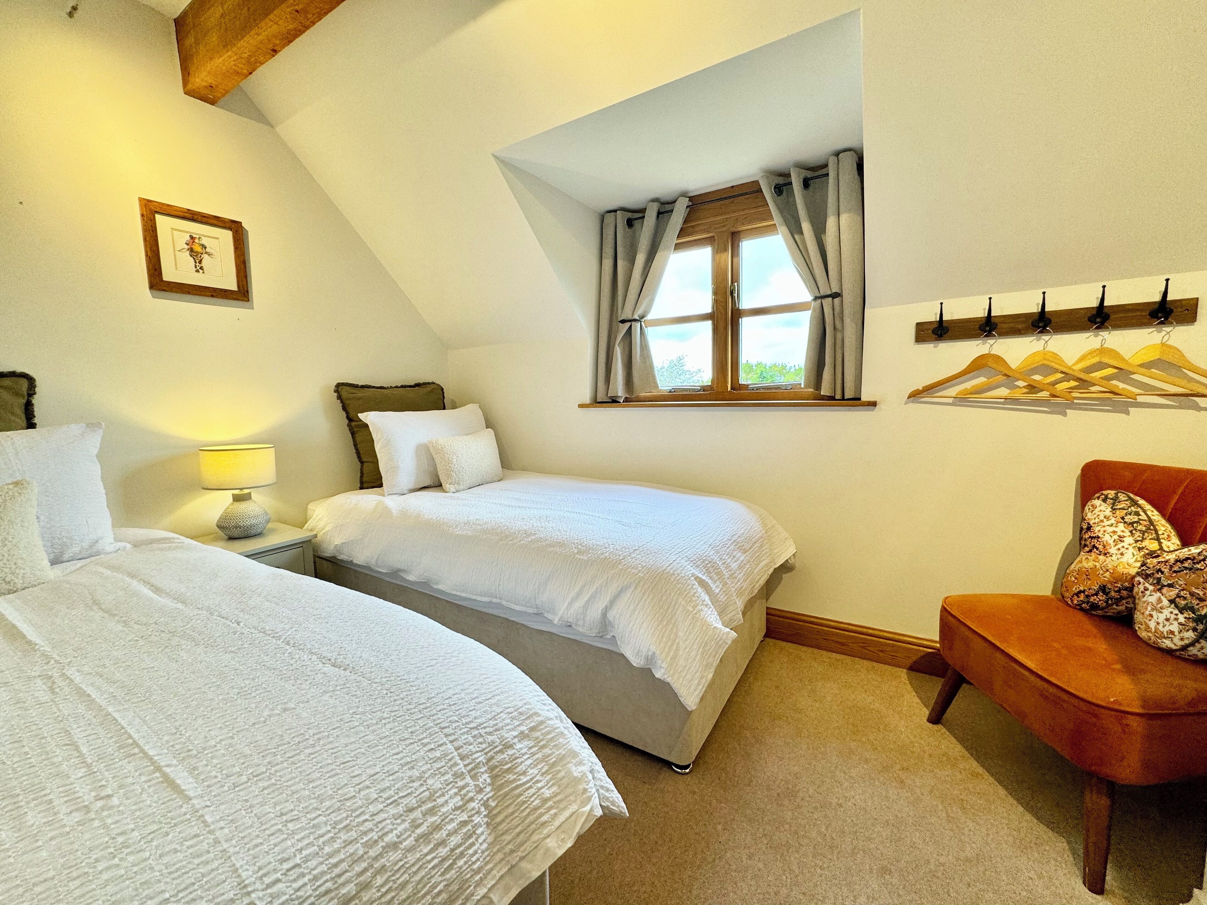 A bedroom with two beds, a window with curtains, a chair, and a coat rack.