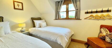 A bedroom with two beds, a window with curtains, a chair, and a coat rack.