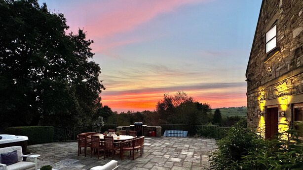 Een terras met buitenmeubilair, een stenen tafel en uitzicht op een zonsondergang.