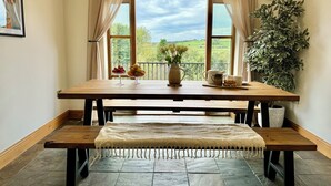 Een eetgedeelte met een houten tafel, banken, uitzicht op groen en een potplant.