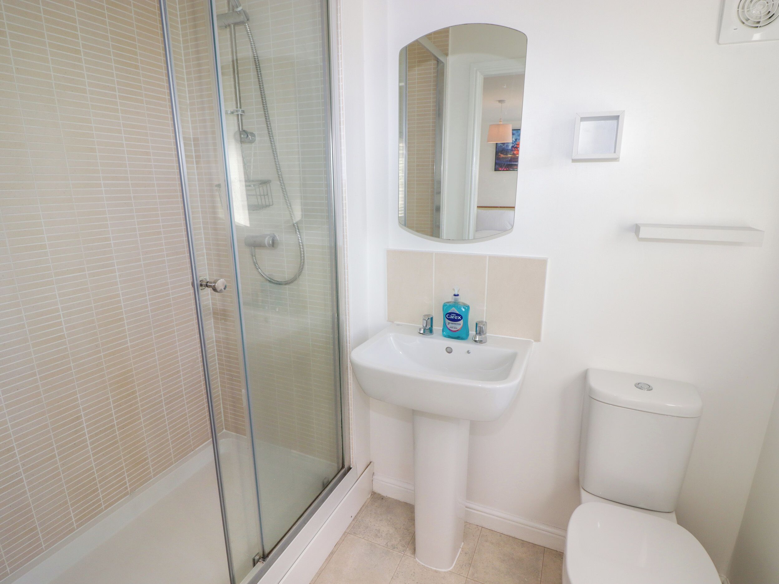 A bathroom with a glass-enclosed shower, a pedestal sink, a toilet, and a mirror above the sink.