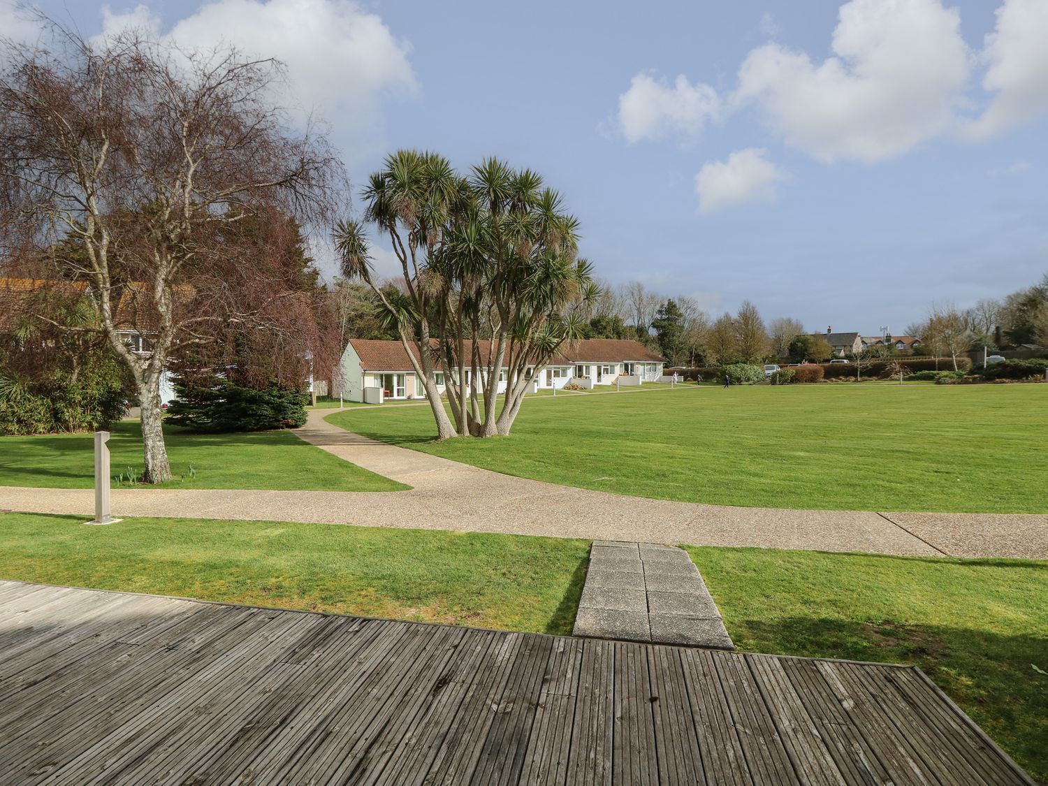 Une zone herbeuse avec une terrasse en bois, un chemin menant à un bâtiment et des arbres.