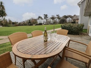 Una mesa redonda de madera con seis sillas de mimbre, una botella de vino y varios vasos en una terraza.