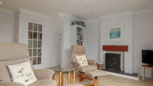 Un salon avec deux fauteuils beiges, une table basse en verre, une cheminée et une bibliothèque.