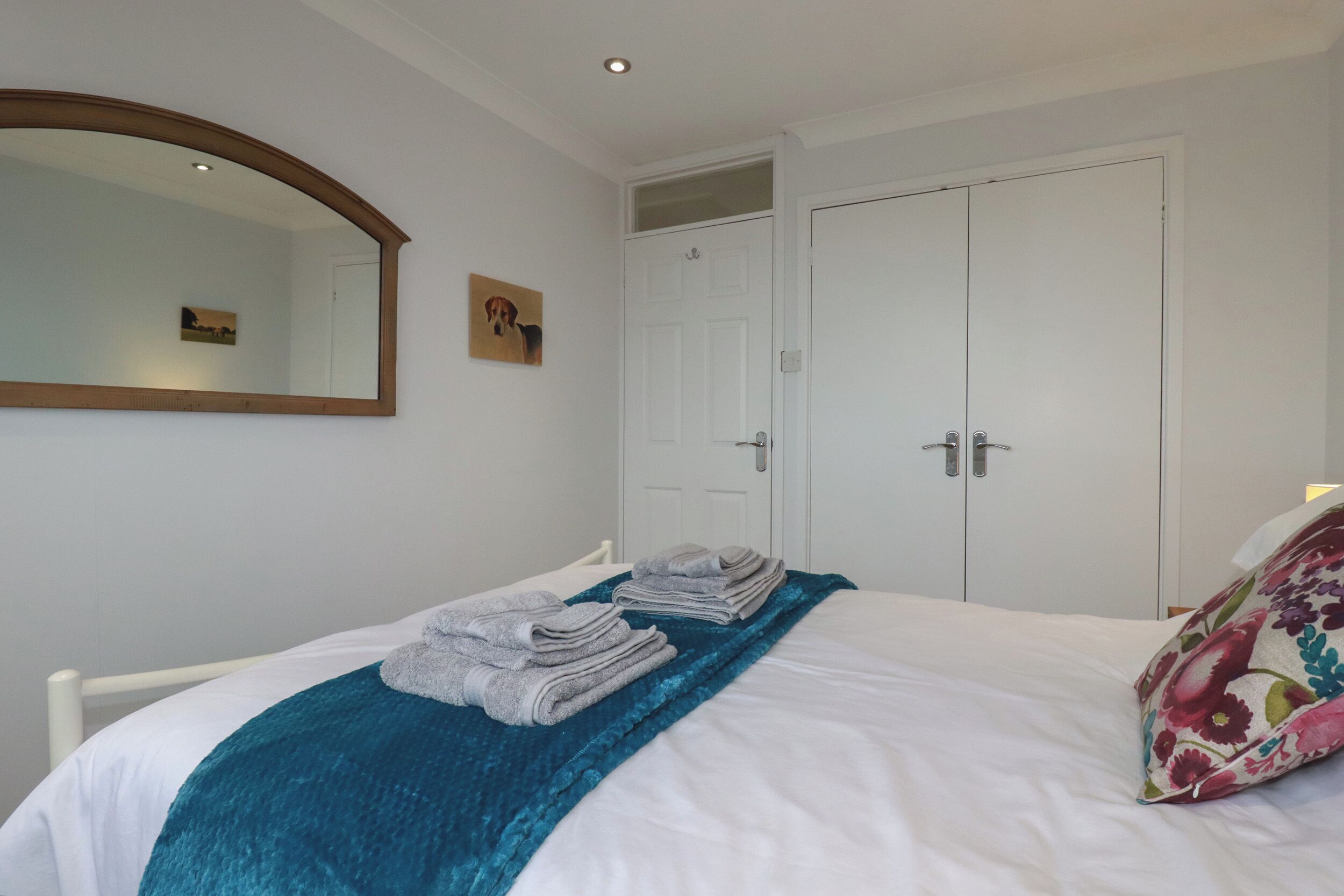 A neatly made bed with folded towels, a teal throw blanket, and a floral pillow.