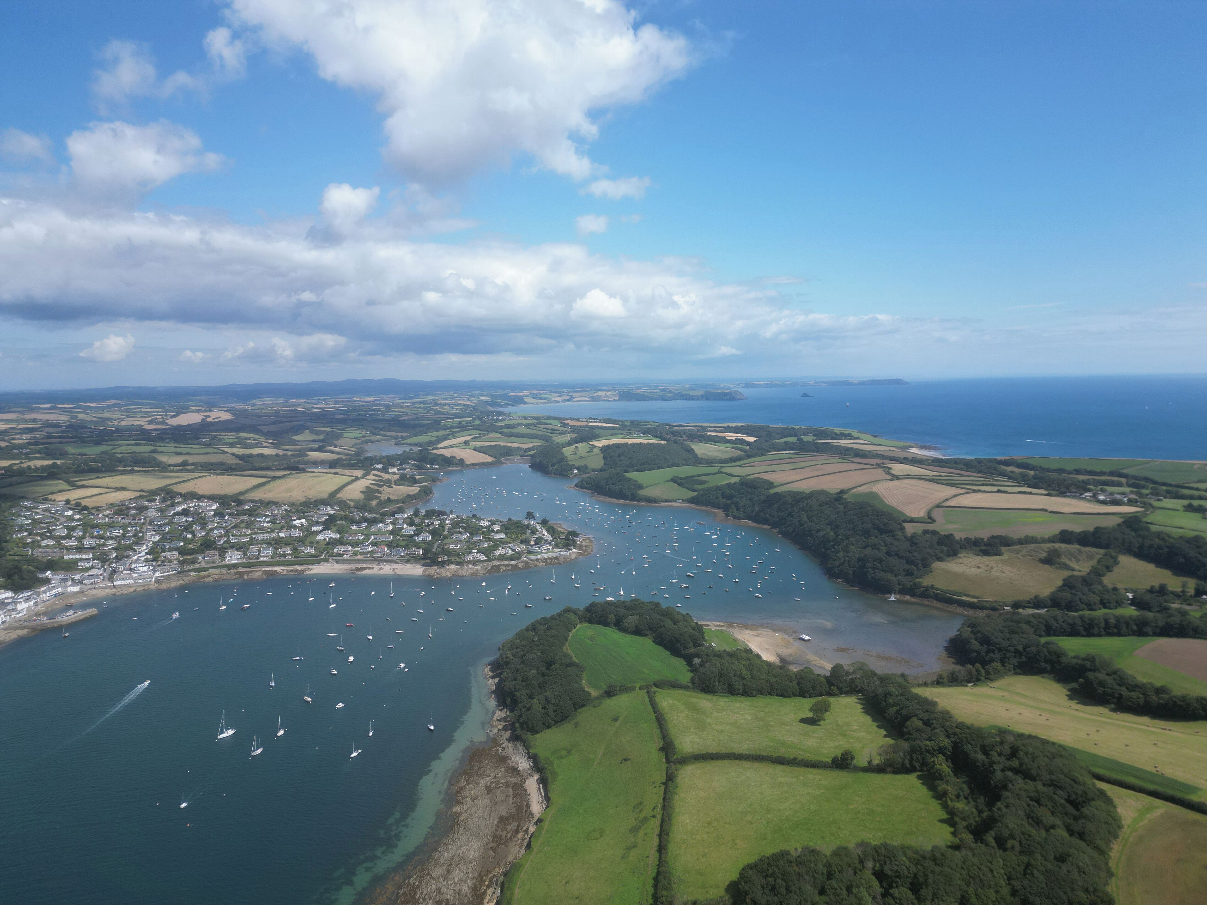 An aerial view of a coastal town with a marina, green fields, and a clear sky.