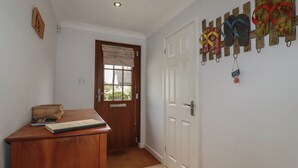 Un couloir avec un bureau en bois, une porte avec une fenêtre et un mur où sont accrochées des paires de tongs.