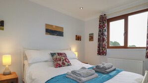 Un lit bien fait, avec une couverture bleue, un coussin à motifs floraux et des serviettes pliées sur une table de chevet en bois.
