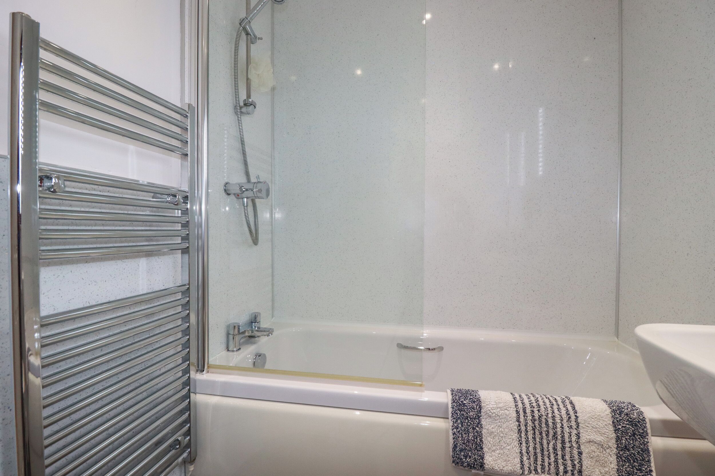 Un baño con ducha envuelta en vidrio, una bañera blanca y una toalla en el suelo.