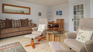 Un salon comprenant un canapé, des fauteuils, une table basse avec un plateau en verre et une table à manger avec des chaises.