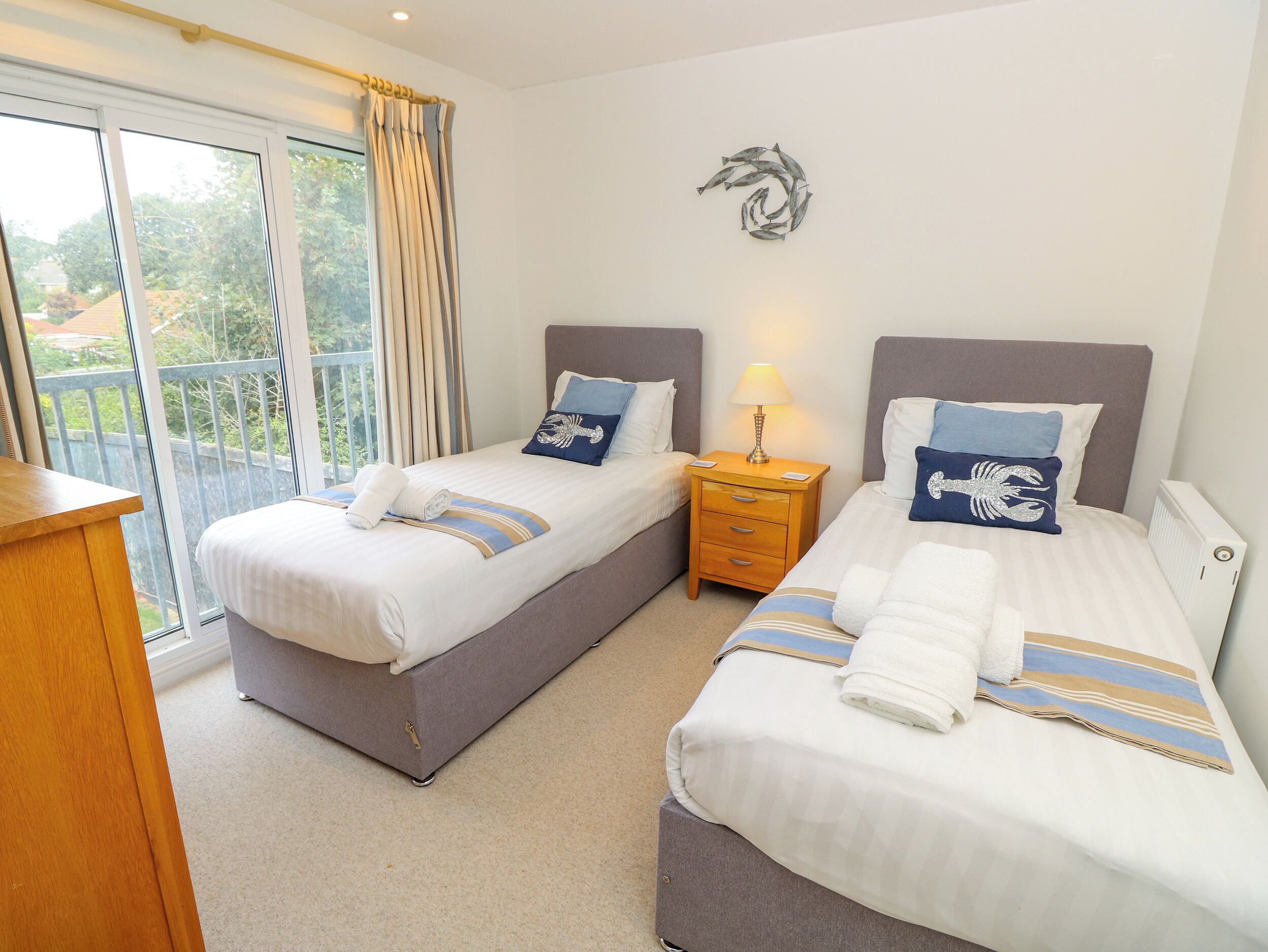 A hotel room with two beds, a nightstand with a lamp, a view through a sliding door, and a decorative wall piece.