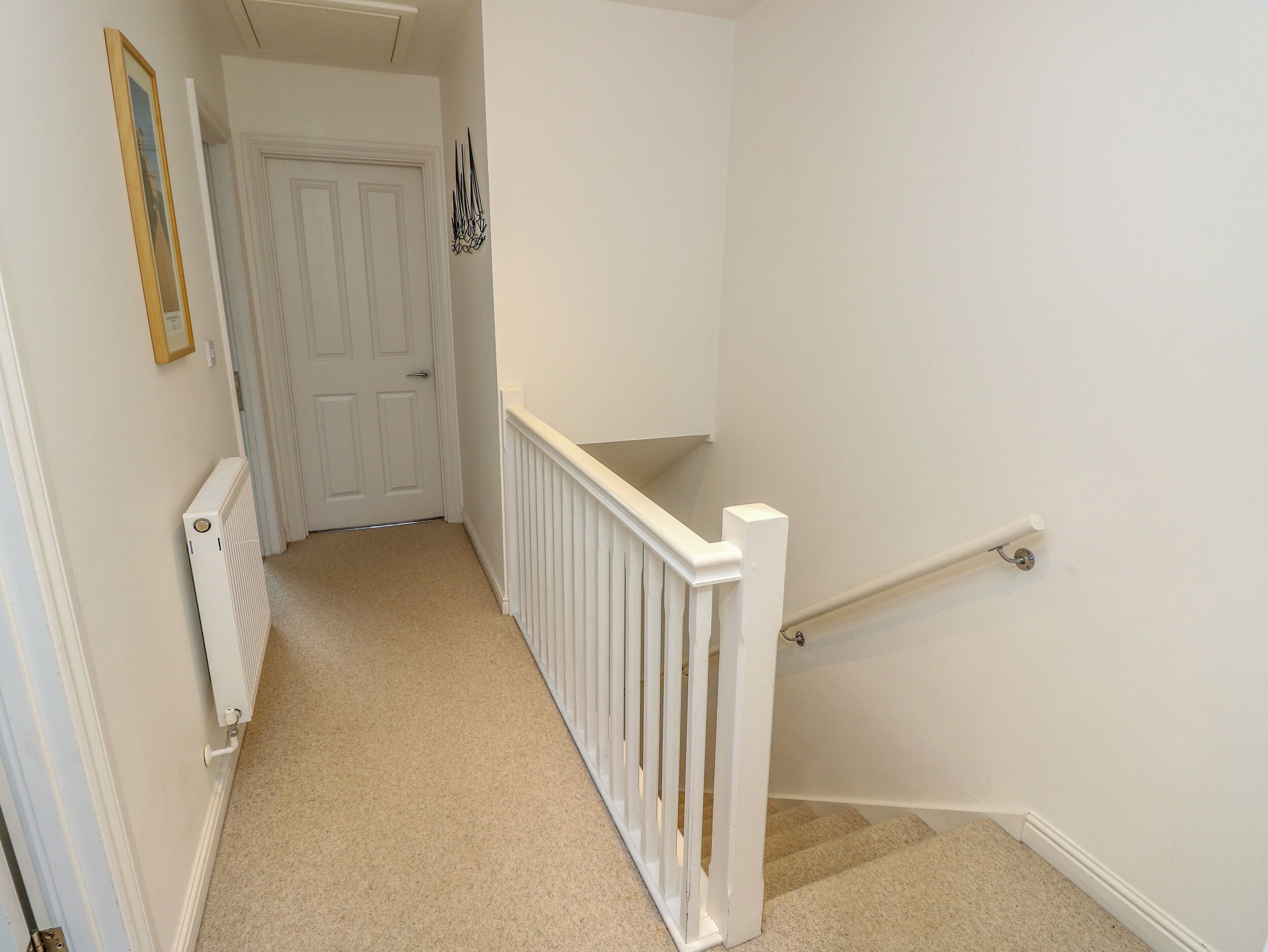 A narrow hallway with a white door at the end, a radiator on the left, and a white railing on the right.