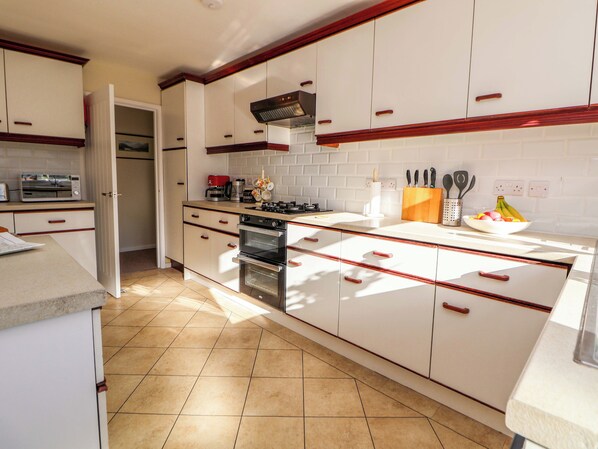 A kitchen with white cabinets, a stove, and a microwave. - Green View (Llangollen)