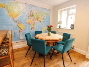 A dining area with a round wooden table, teal upholstered chairs, a leopard print chair, and a world map on the wall. - Garden Retreat (Swanage)