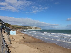 A beach with a building on the left, a cliff in the background, and the sea in the middle. - Garden Retreat (Swanage)