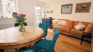 Een eetgedeelte met een houten tafel en teal-kleurige stoelen, een bank met een steroefenkussen en kunst aan de muur.