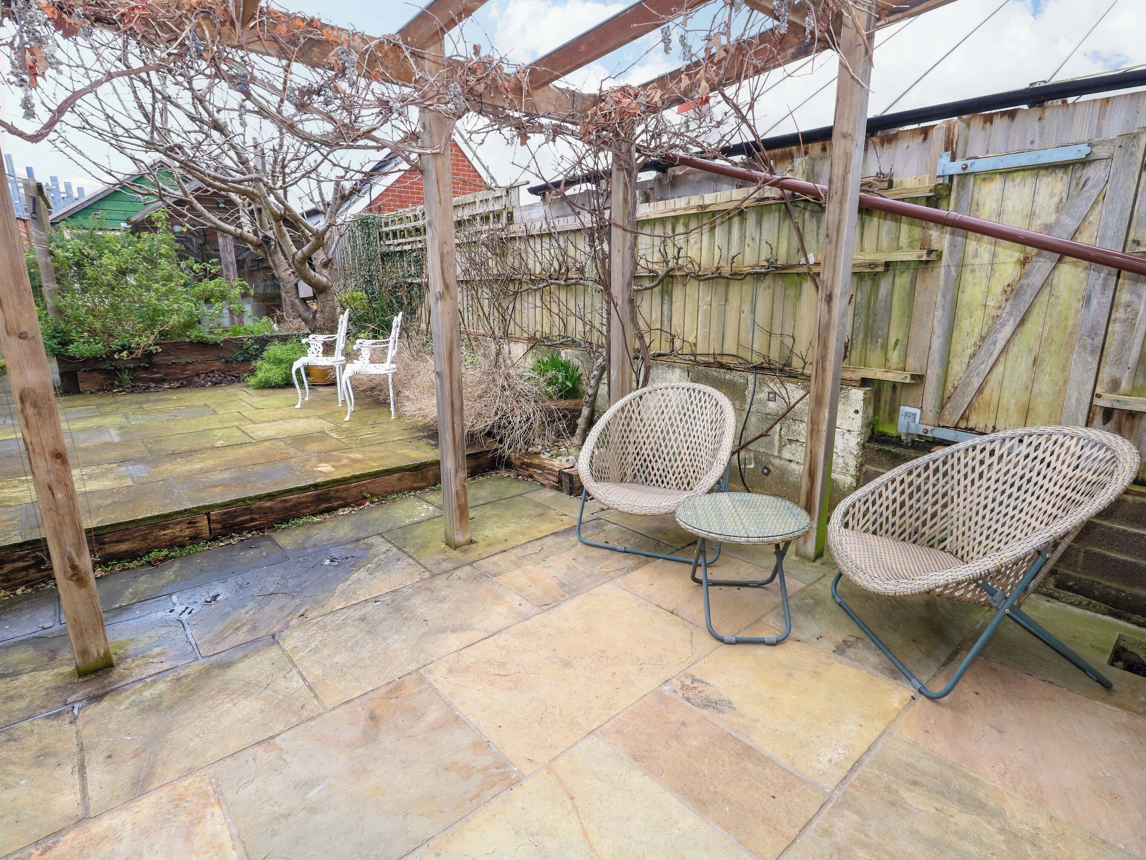 A patio area with stone flooring, two wicker chairs, and a wooden pergola.