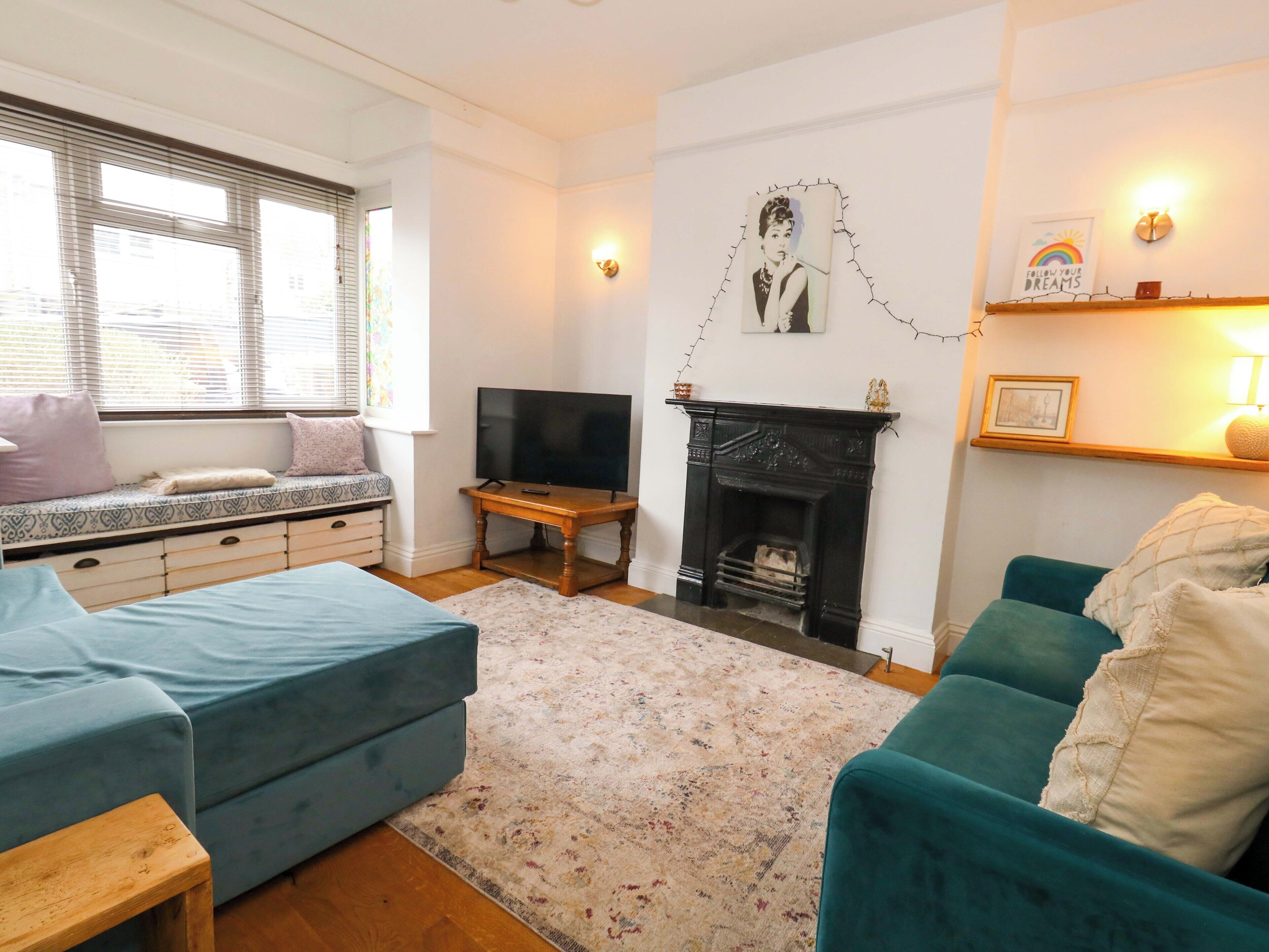 A living room with a sofa, a television, a fireplace, and a window with blinds.