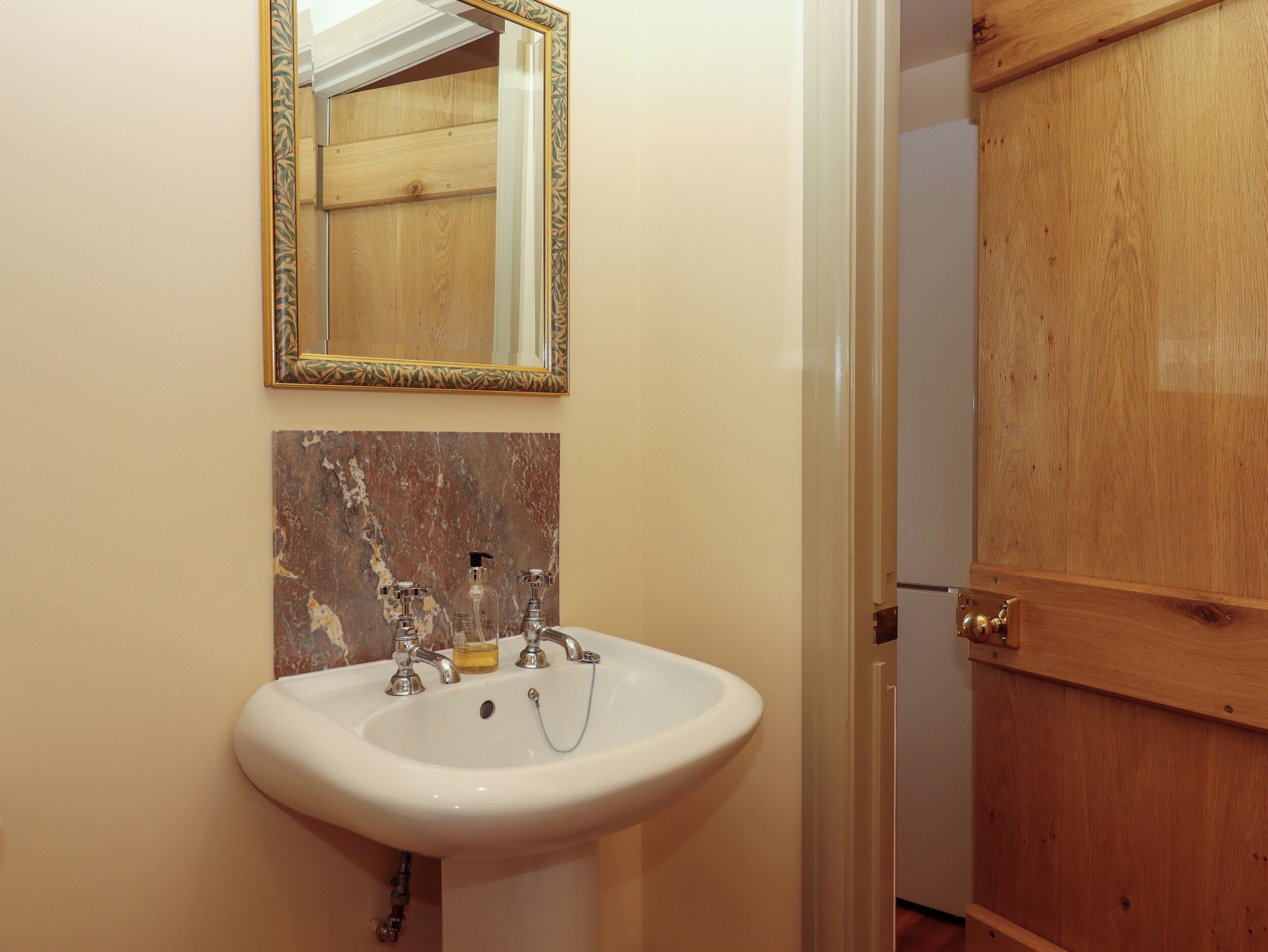 A bathroom with a white sink, a mirror with a decorative frame, and a wooden door.