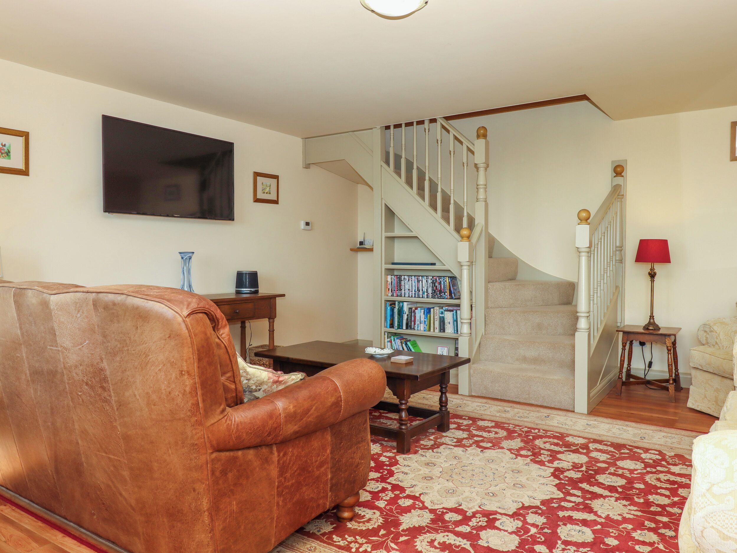 A living room with a brown leather sofa, a coffee table, a bookshelf, and a staircase.