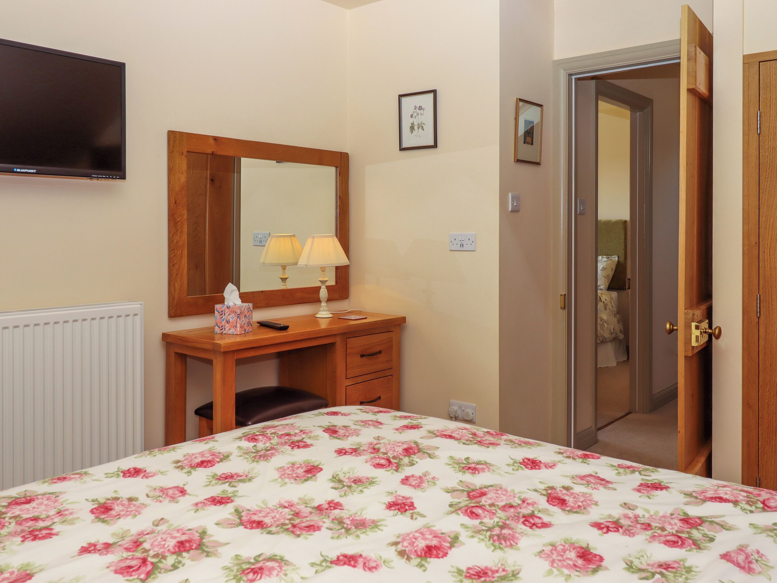 A hotel room with a bed, a desk with a mirror, a lamp, and a television on the wall.