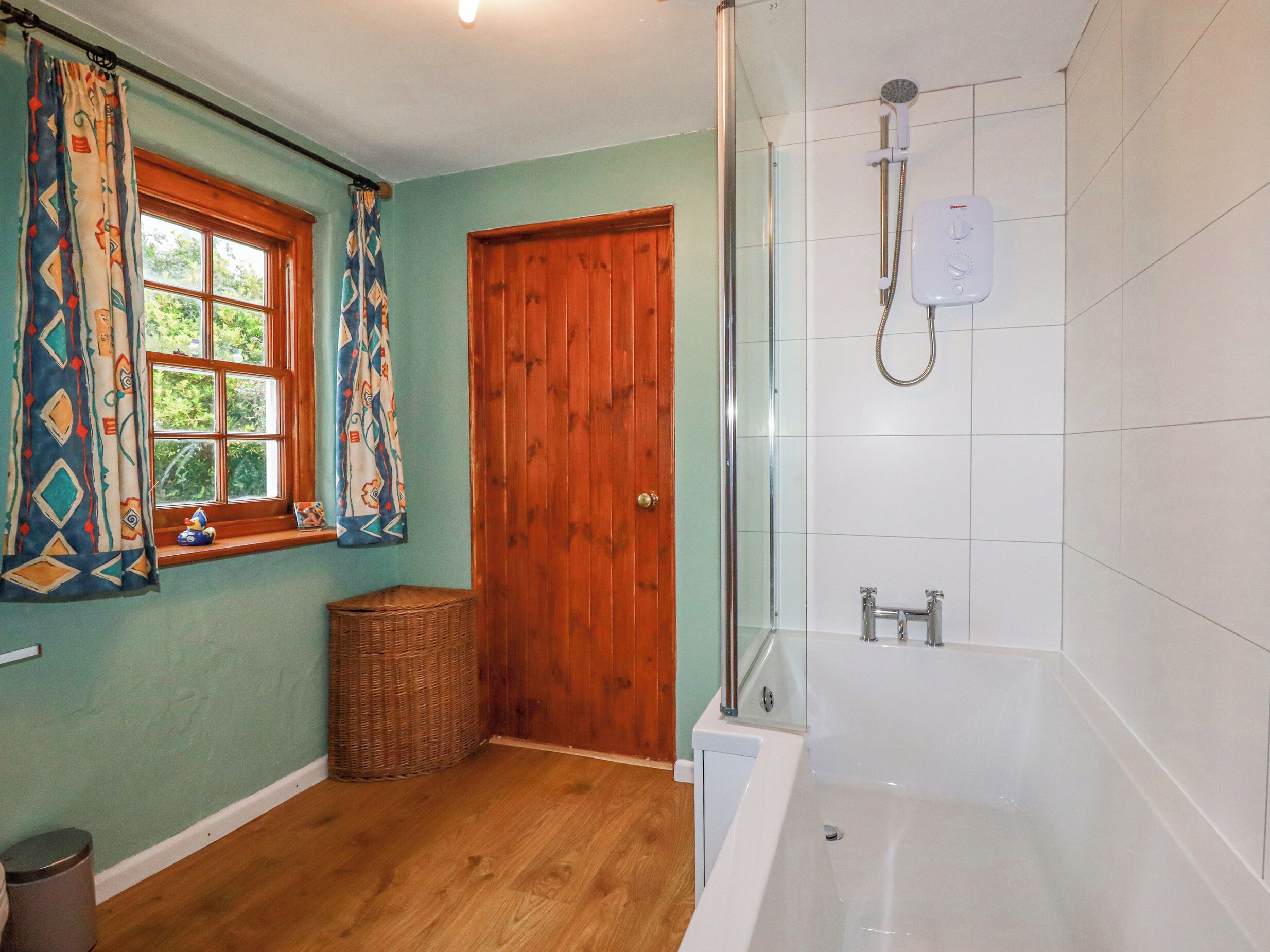A bathroom with a bathtub, a shower, a window with curtains, and a wooden door.