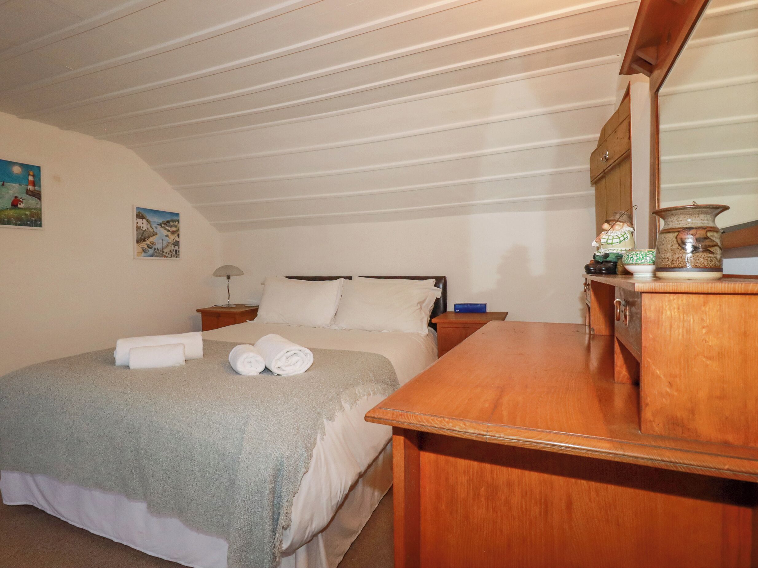 A bedroom with a bed, a wooden dresser, a nightstand, and a mirror.