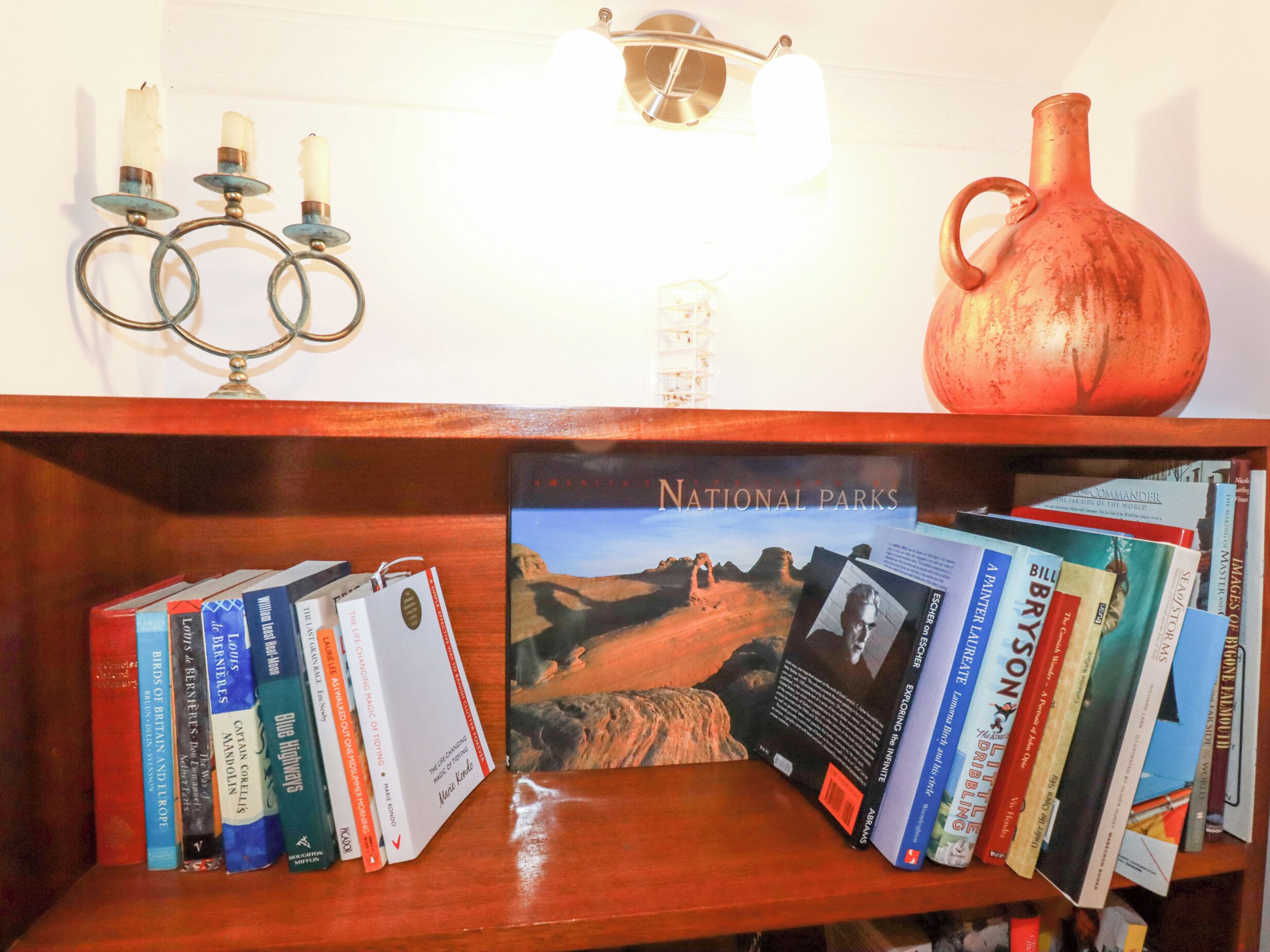A bookshelf with books, a National Parks brochure, a candle holder, and a vase.