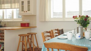 A kitchen with white cabinets, a red pot on the counter, and a dining area with a table set for two. - Trestar (Wadebridge)