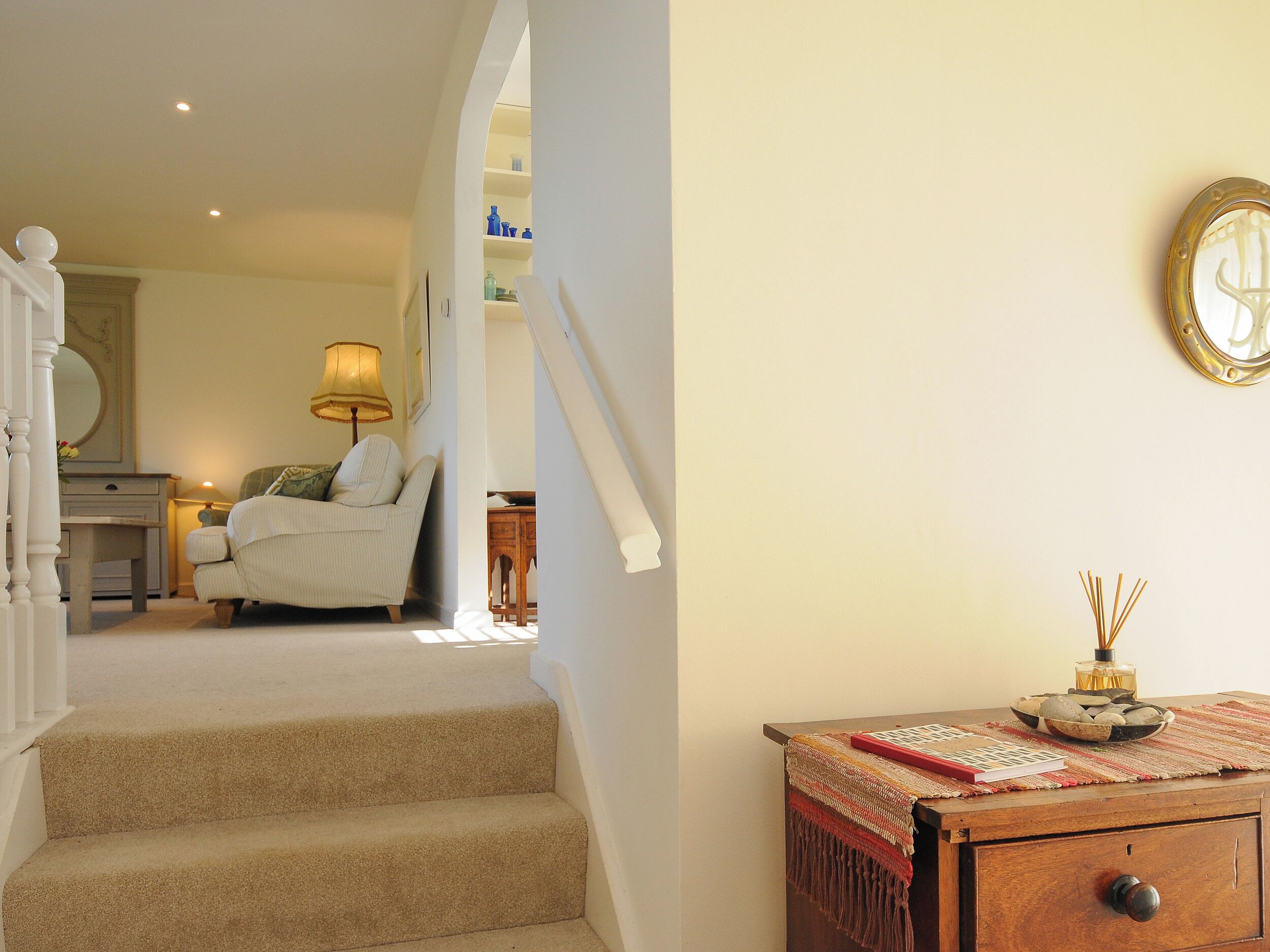 A staircase leading to a bedroom with a bed, a nightstand, and a lamp. There is a wooden dresser with a decorative item on top.