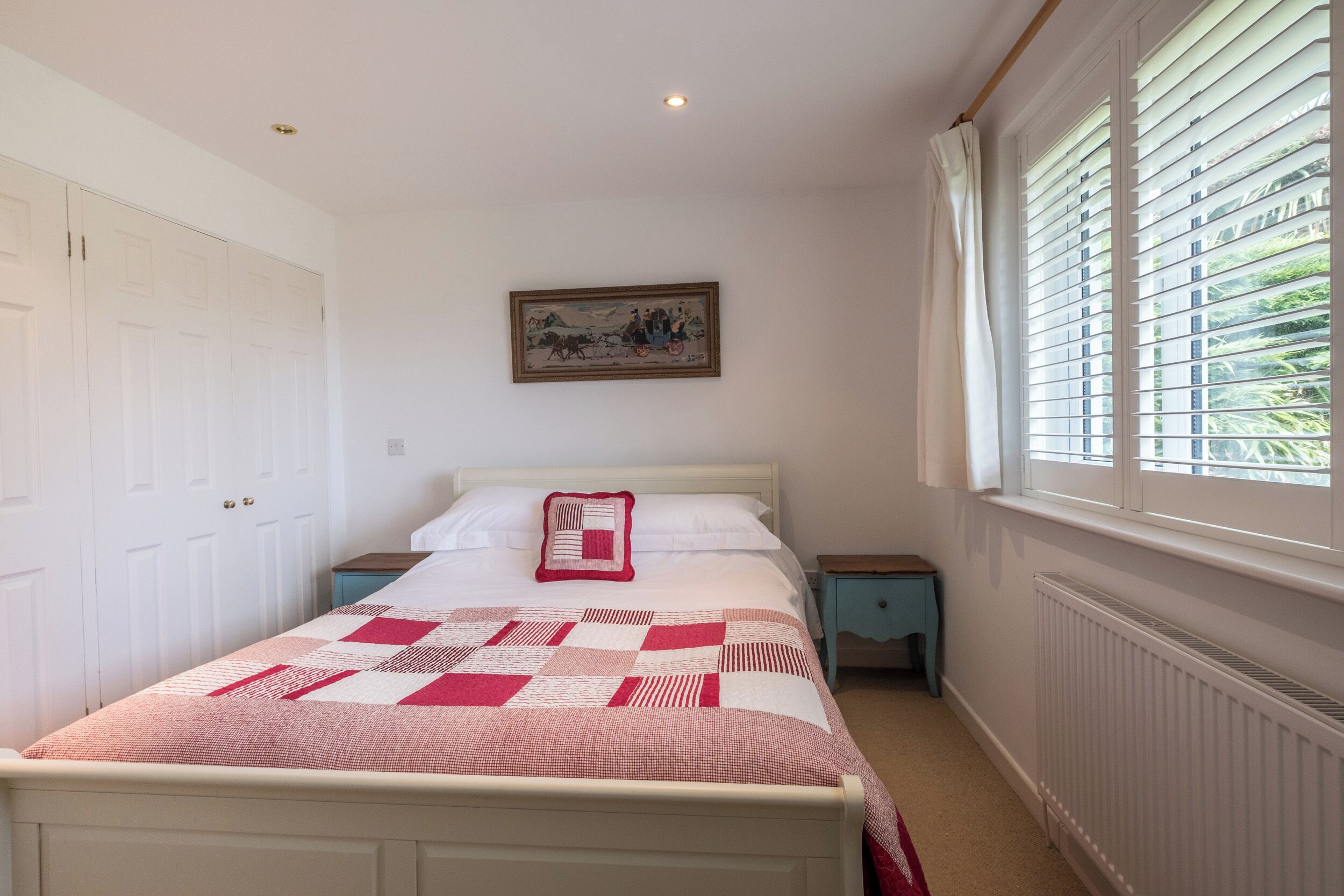 A bedroom with a bed, a nightstand, a dresser, a window with blinds, and a painting on the wall.
