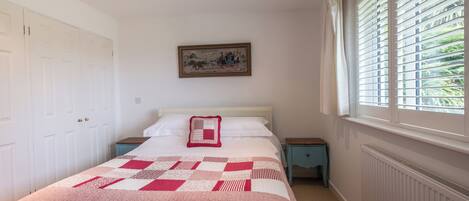 A bedroom with a bed, a nightstand, a dresser, a window with blinds, and a painting on the wall.