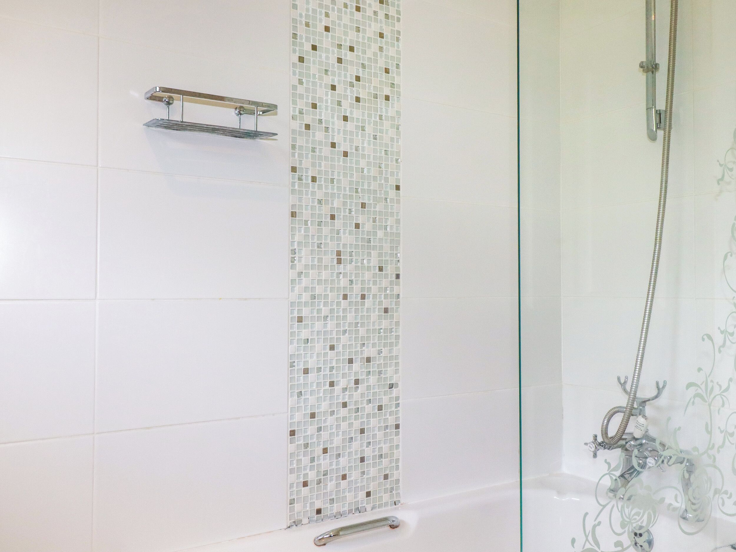 A bathroom with white tiles, a glass shower enclosure, and a showerhead.