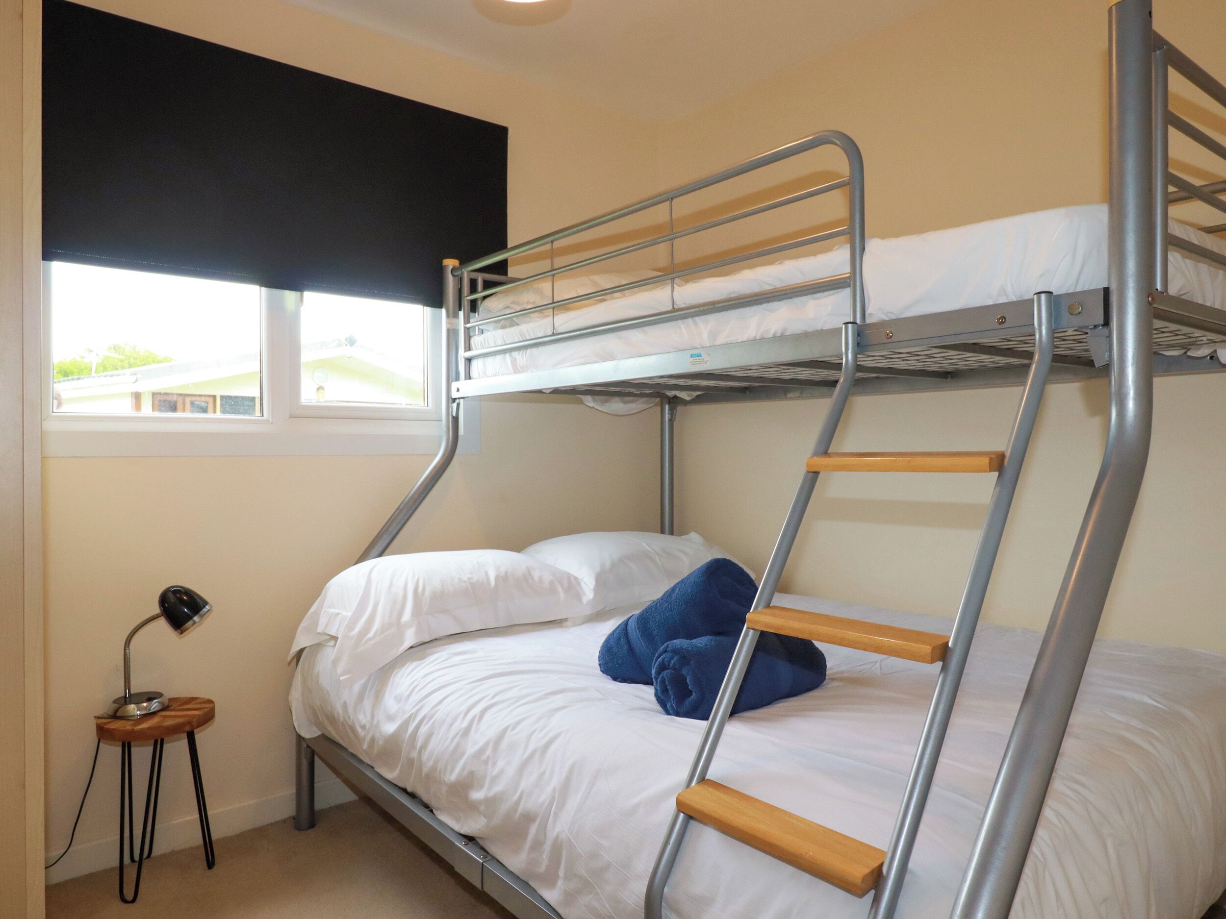 A bunk bed room with a window, a desk, and a lamp.